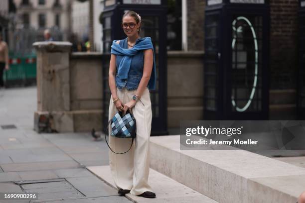 Fashion week guest was seen wearing brown leather shoes, wide beige trousers, lots of yellow gold jewelry, a silver rolex, red transparent shades, a...