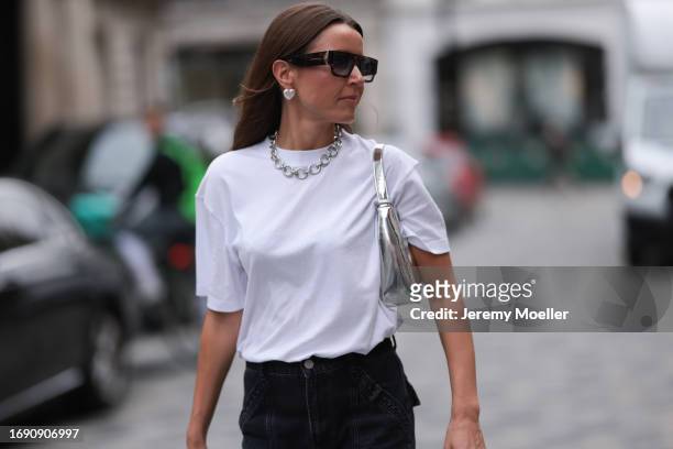 Fashion week guest was seen wearing a dark denim jeans, a white top along with a silver chain and a shiny silver bag, silver rings, silver heart...