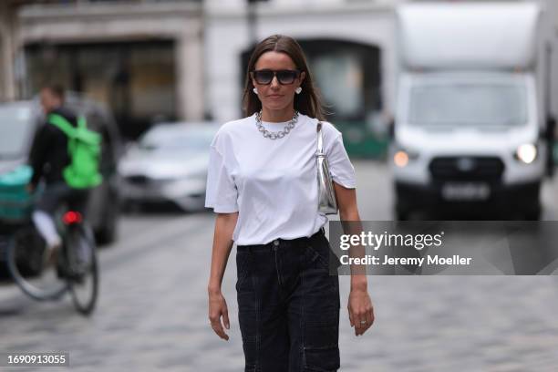 Fashion week guest was seen wearing a dark denim jeans, a white top along with a silver chain and a shiny silver bag, silver rings, silver heart...