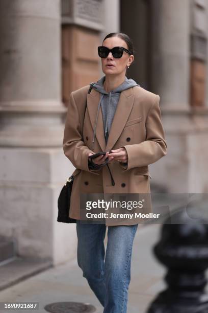 Fashion week guest was seen wearing a denim jeans, a grey pullover, dark shades, a black bag and a broen jacket with dark brown buttons on it before...