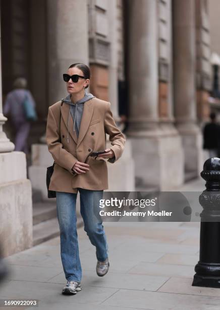 Fashion week guest was seen wearing silver sneaker, a denim jeans, a grey pullover, dark shades, a black bag and a broen jacket with dark brown...