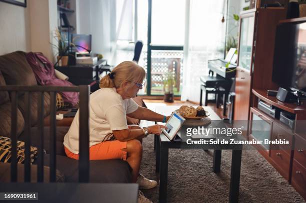 senior woman using digital tablet in living room - photo de film stock pictures, royalty-free photos & images