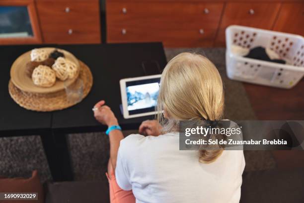 senior woman using digital tablet in living room - photo de film stock pictures, royalty-free photos & images