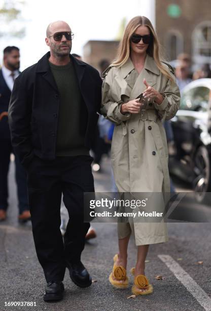Jason Statham was seen wearing black shoes, black pants, a green pullover, a black jacket and dark shades next to Rosie Huntington-Whiteley wearing...
