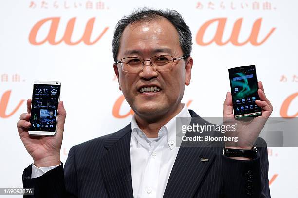 Takashi Tanaka, president of KDDI Corp., holds the company's au brand smartphones HTC J One HTL22, manufactured by HTC Corp., left, and Urbano L01,...
