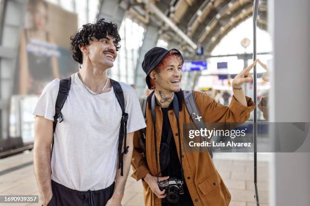 gay couple checking route map on subway train platform - departure board front on fotografías e imágenes de stock