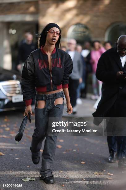 Fashion Week guest was seen wearing black leather boots, grey jeans with two holes on the legs, a black leather bag, a cropped black and red Movalola...