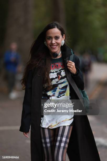 Fashion Week guest was seen wearing black leather boots, brown and white checked Burberry pants, a black Burberry coat, a colorful tshirt with...