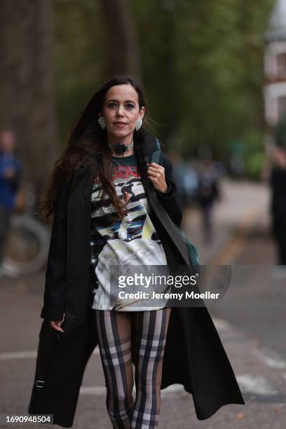 Fashion Week guest was seen wearing black leather boots, brown and white checked Burberry pants, a black Burberry coat, a colorful tshirt with...
