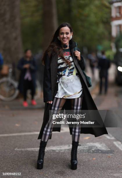 Fashion Week guest was seen wearing black leather boots, brown and white checked Burberry pants, a black Burberry coat, a colorful tshirt with...