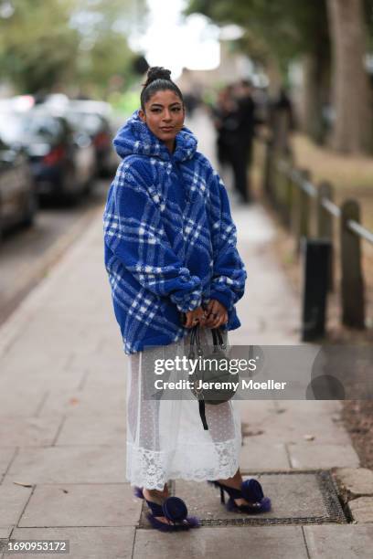 Fashion Week guest was seen wearing purple Burberry sandals with a rose on top, a transparent white dress under an oversized blue and white checked...