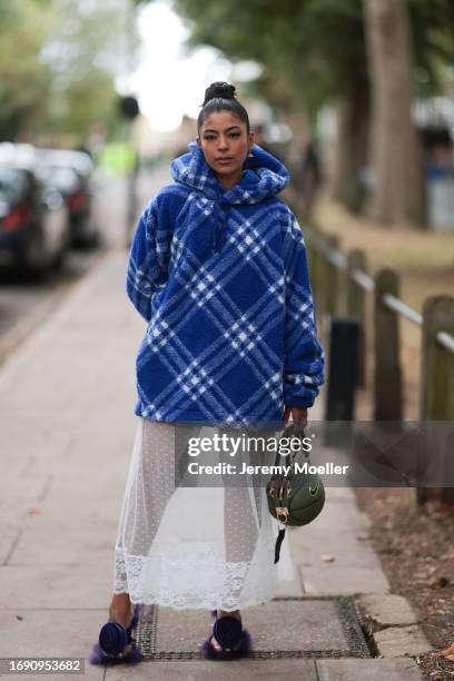 Fashion Week guest was seen wearing purple Burberry sandals with a rose on top, a transparent white dress under an oversized blue and white checked...