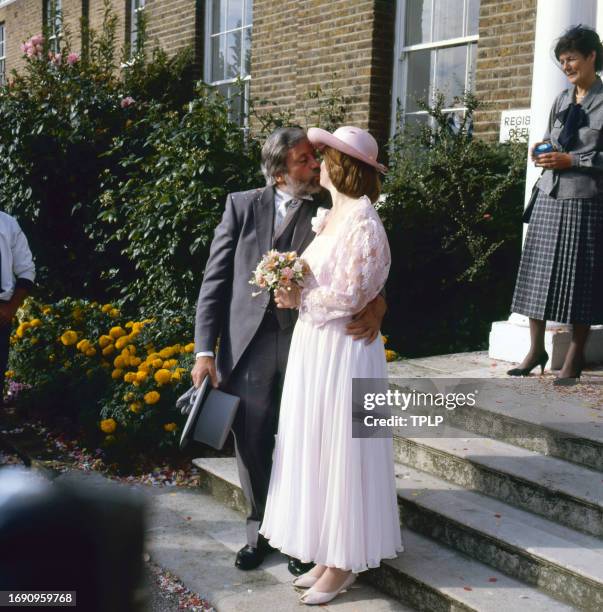 View of couple actor Oliver Reed and Josephine Burge as they kiss during their wedding, Surrey, England, July 9, 1985.