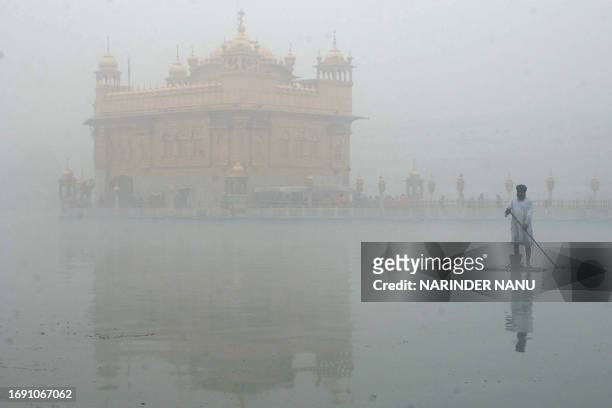 An Indian Sikh man cleans the water tank during morning fog at the Golden Temple in Amritsar on February 5, 2008. Dense fog and cold temperatures...