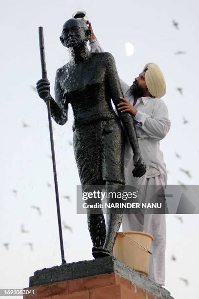 Indian devotee Sawraj Singh gives a milk bath to a statue of Mahatma Gandhi in Amritsar, 01 October 2006, on the eve of the birth anniversary of...