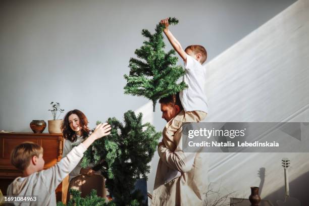 family with two children assembles christmas tree from several parts, and together they place top of tree on its base. - home base stockfoto's en -beelden