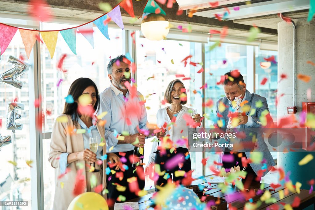 Empresarios maduros celebrando con popper de fiesta de confeti en la oficina