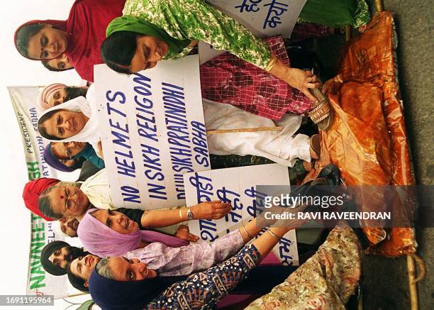 Sikh woman stomp their footwear upon a mock coffin with wrapped helmets during 06 November protest against a new law ordering all people travelling...