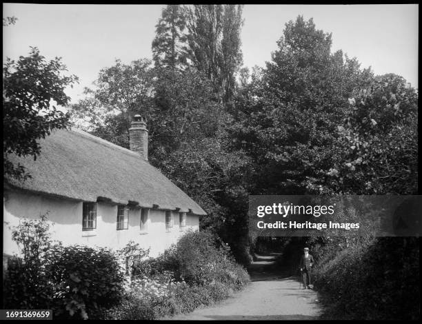 Dunster, West Somerset, Somerset, 1940-1953. View of a lane in Dunster with a low thatched cottage on the left and a man stood on the right side of...