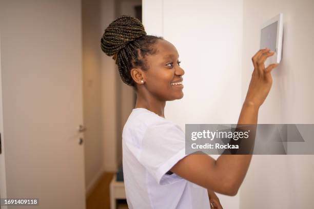 young woman adjusts the temperature at home with a device on the wall - smart thermostat stock pictures, royalty-free photos & images