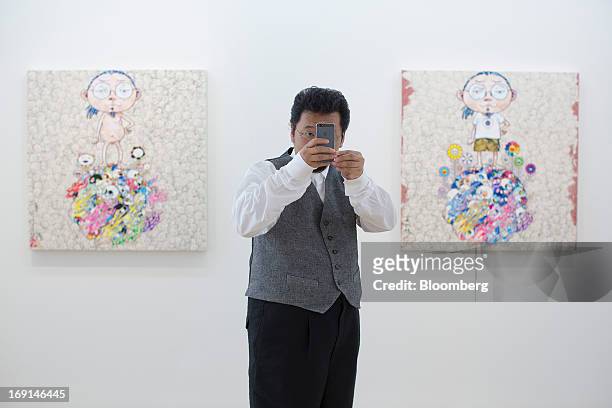 Takashi Murakami, a Japanese contemporary artist, takes a photograph with a smartphone in front of his paintings on exhibit at the Galerie Perrotin...