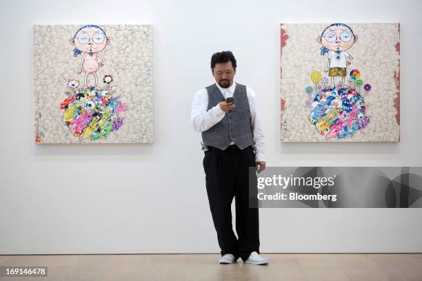 Takashi Murakami, a Japanese contemporary artist, uses a smartphone in front of his paintings on exhibit at the Galerie Perrotin in Hong Kong, China,...