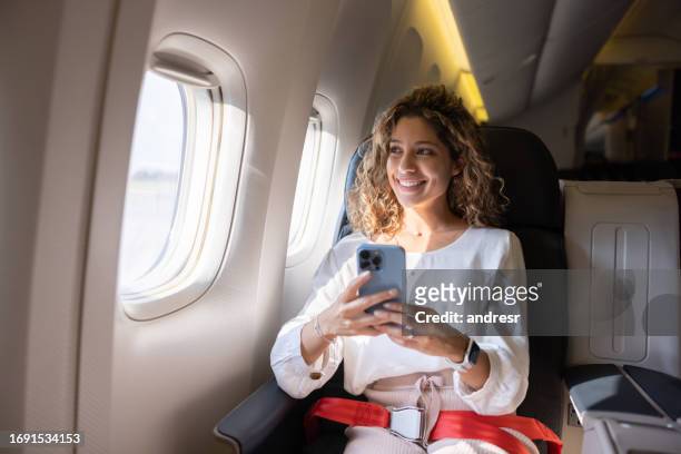 female traveler using her cell phone in an airplane - airplane seat stock pictures, royalty-free photos & images