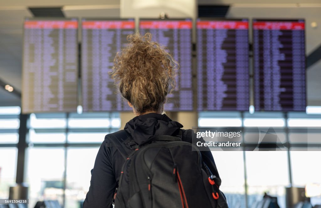 Viaggiatore all'aeroporto che guarda il tabellone di partenza di arrivo
