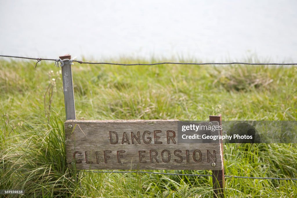 A wooden sign warning of the danger of cliff erosion at the top of the sheer cliffs at Beachy Head, East Sussex, England