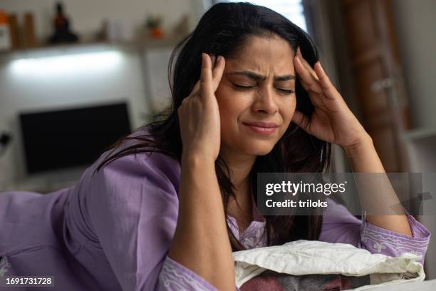 femme se touchant la tête de douleur et allongée sur son lit - mal de tête photos et images de collection
