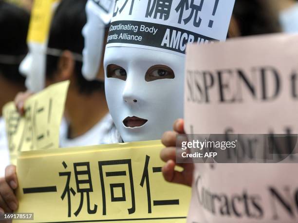 Foreign domestic helper, wearing a mask to conceal her identity from her employer, demonstrates with others outside the Government Central Offices in...