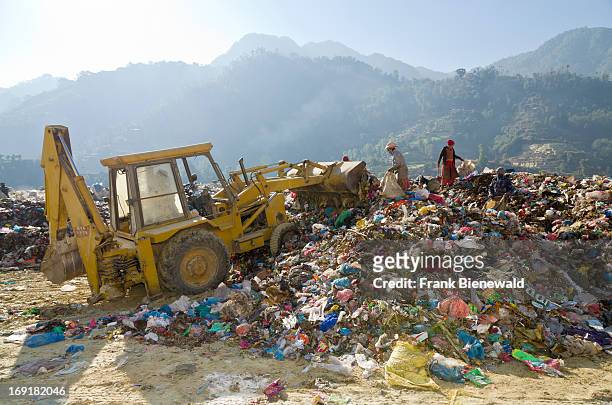 Bucket excavator shoving garbage into a heap, while two workers look for recyclable material, at the Aletar garbage dump. The garbage collected off...