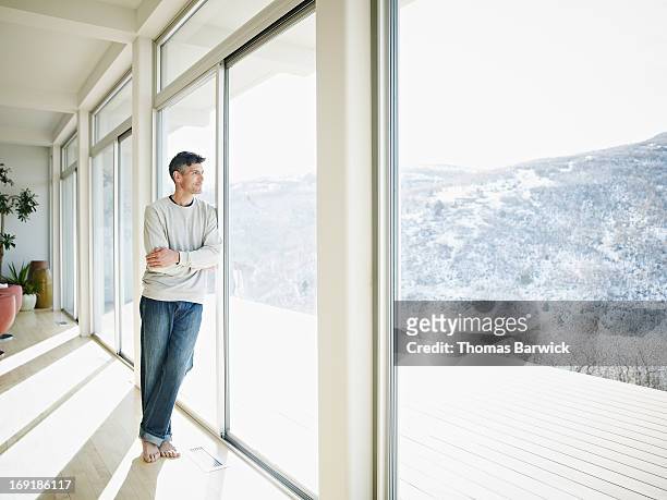 mature man looking out windows of modern home - finestra foto e immagini stock