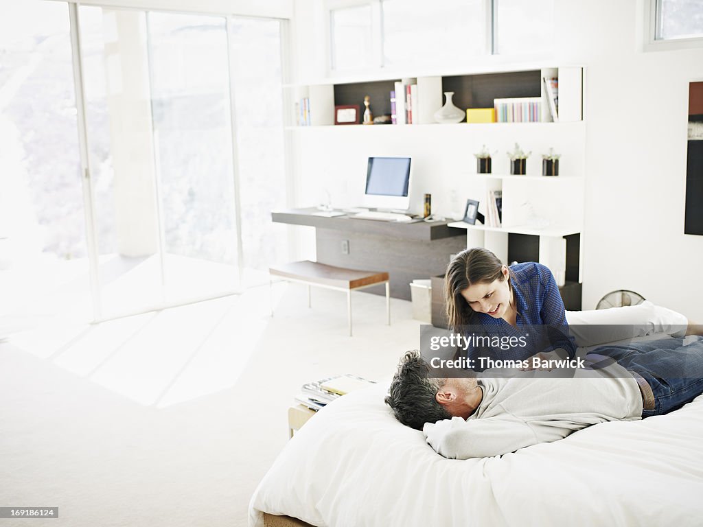 Smiling couple lying on bed in modern home talking