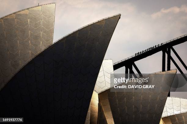 Tourists climb the Sydney Harbour Bridge behind the Sydney Opera House on September 27, 2023.