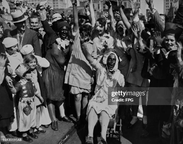 Mardi Gras revellers in costume, two people wear blackface with others wearing masks, many with their arms raised in celebration during the annual...