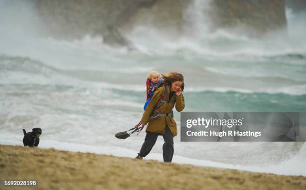 Woman takes a child and dog for a walk in front of stormy waves at Gyllyngvase Beach on September 20, 2023 in Falmouth, England. Parts of England are...