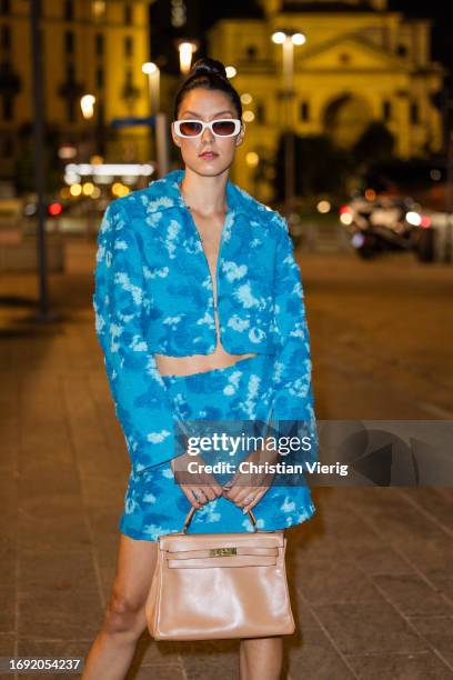 Rebecca Mir wears blue jacket and skirt with print, brown Hermes bag, white socks, shoes, sunglasses during the Milan Fashion Week - Womenswear...