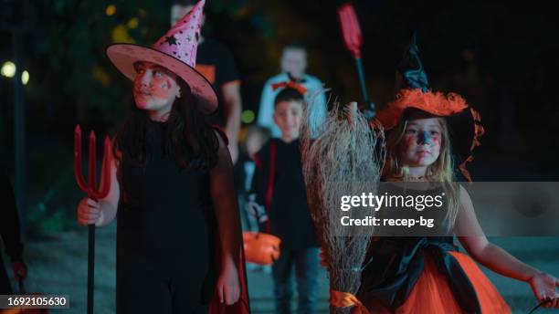 group of children friends visiting houses for halloween candies with parents at night - halloween stockfoto's en -beelden