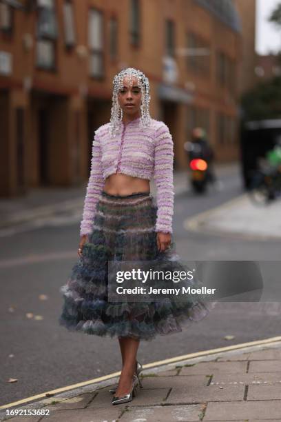 Beka Prance was seen wearing silver shoes, a grey and blue and green transparent skirt, a cropped rose jacket, a silver bag and several round glasses...