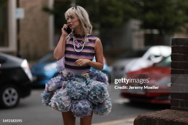 Betty Bachz was seen wearing a wide fluffy skirt in white, blue, green and purple, a shirt striped in purple and rose as well as colorful chains in...