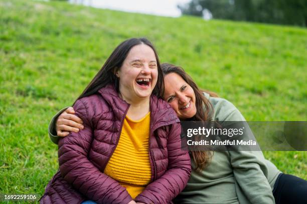 woman with down syndrome laughing while sitting in grass with mother - down syndrome stock pictures, royalty-free photos & images