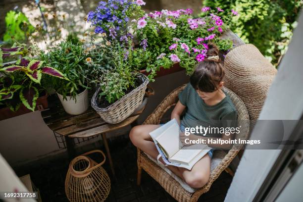 young girl reading a book on the balcony, surrounded by colorful balcony flowers. - urban garden stock pictures, royalty-free photos & images