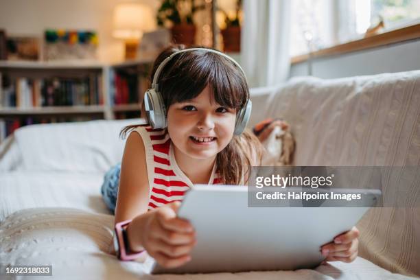 portrait of a young girl watching a video on a tablet with wireless headphones on. girl spending her summer indoors, online, and alone. - multimedia learning stock pictures, royalty-free photos & images