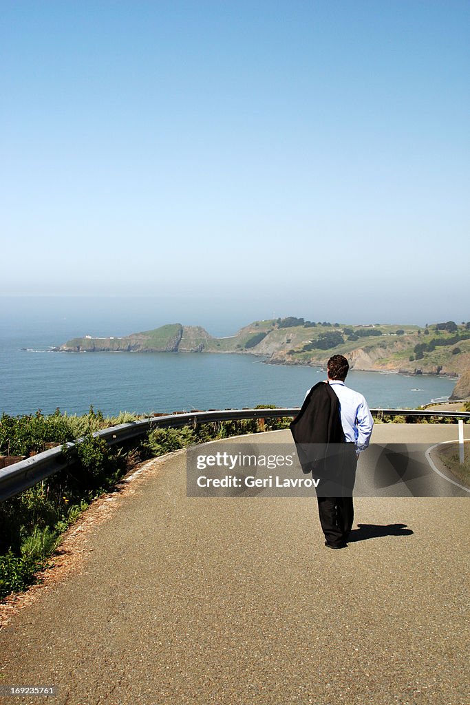 Man in a suit walking on a coastal road