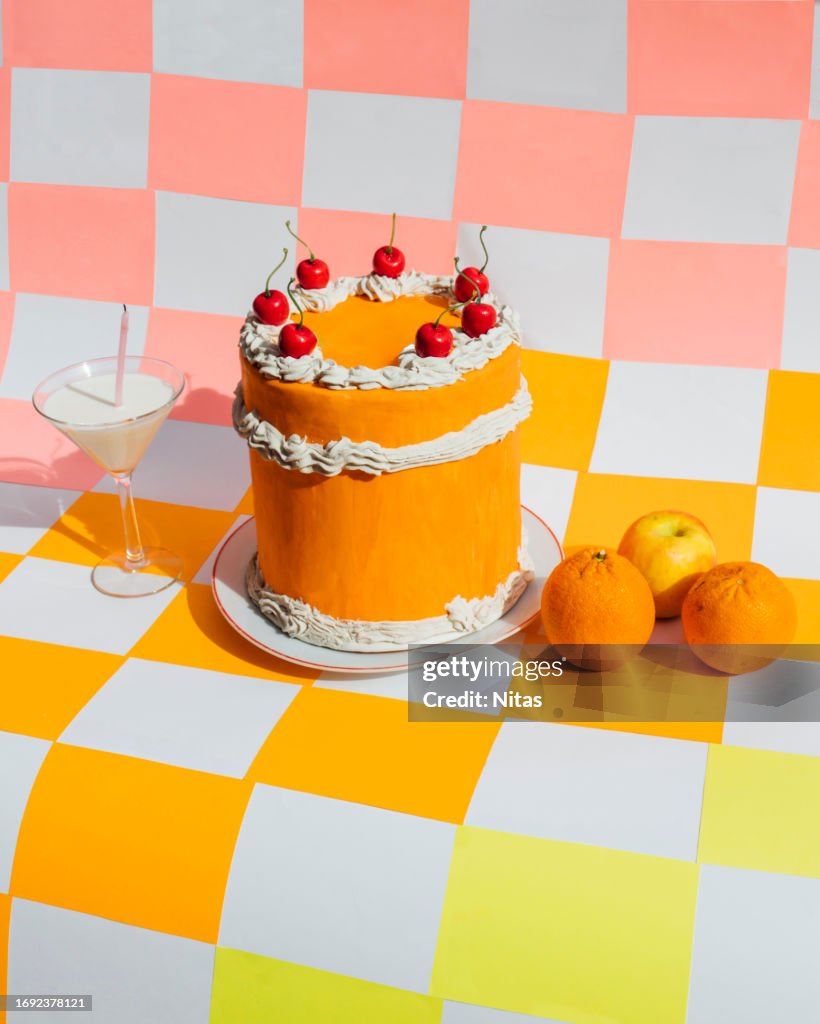 Orange cake with milk cocktail and citric fruit on multicolored checkered background