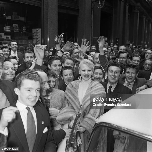 British actress Sabrina , stands in a street surrounded by male admirers while on a visit to the London Stock Exchange, London, April 29th, 1958.