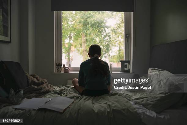 powerful portrait of a young girl looking out of her bedroom window on a gloomy day - achterhoofd stockfoto's en -beelden