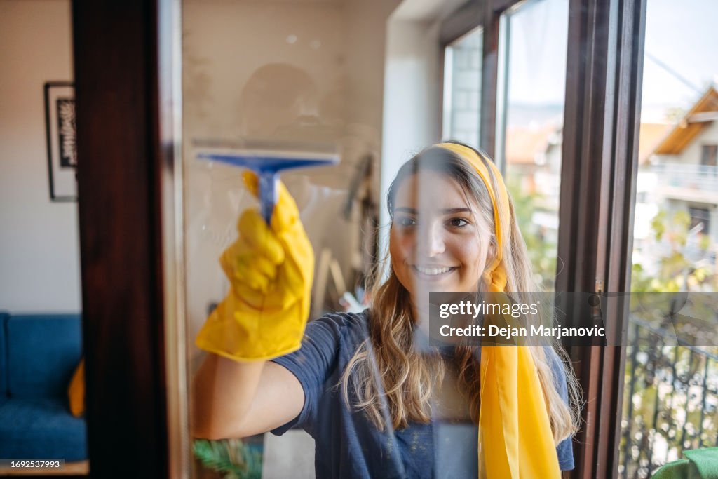 Girls cleaning window in living room together