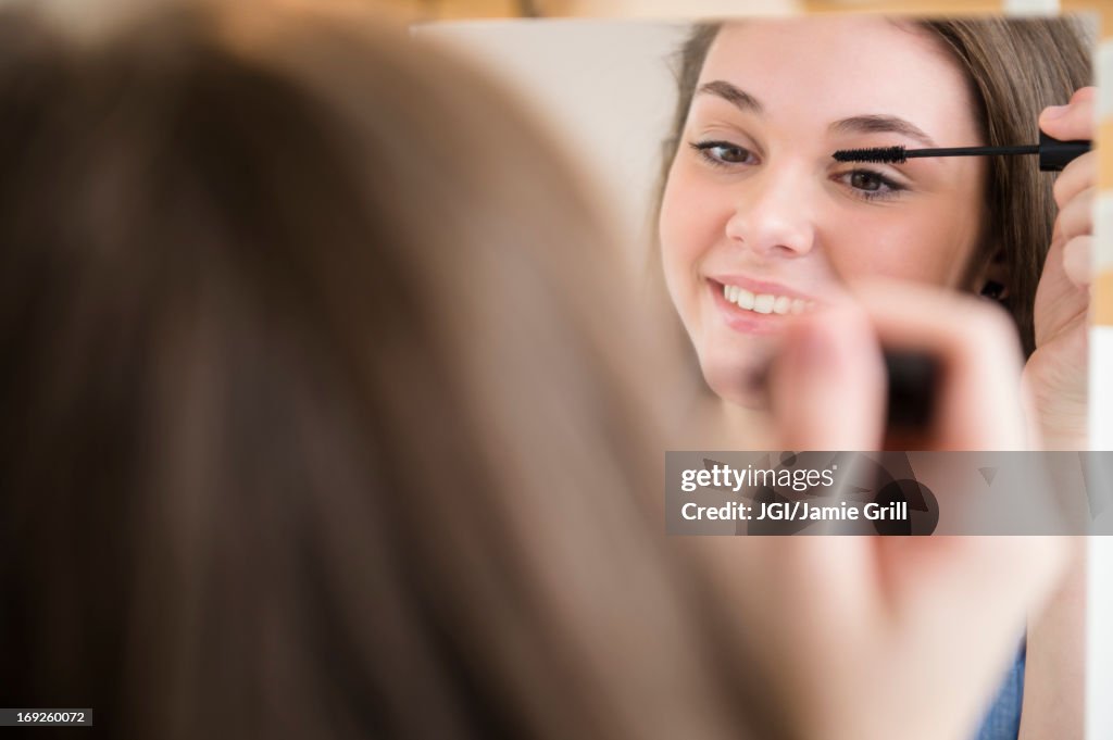 Hispanic girl applying makeup in mirror